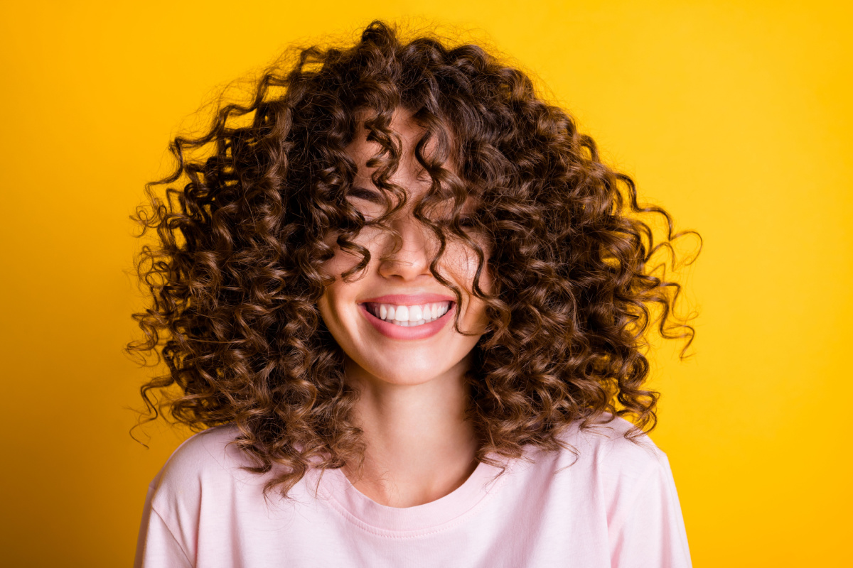 Mulher sorridente de cabelo castanho cacheado cortado nos ombros